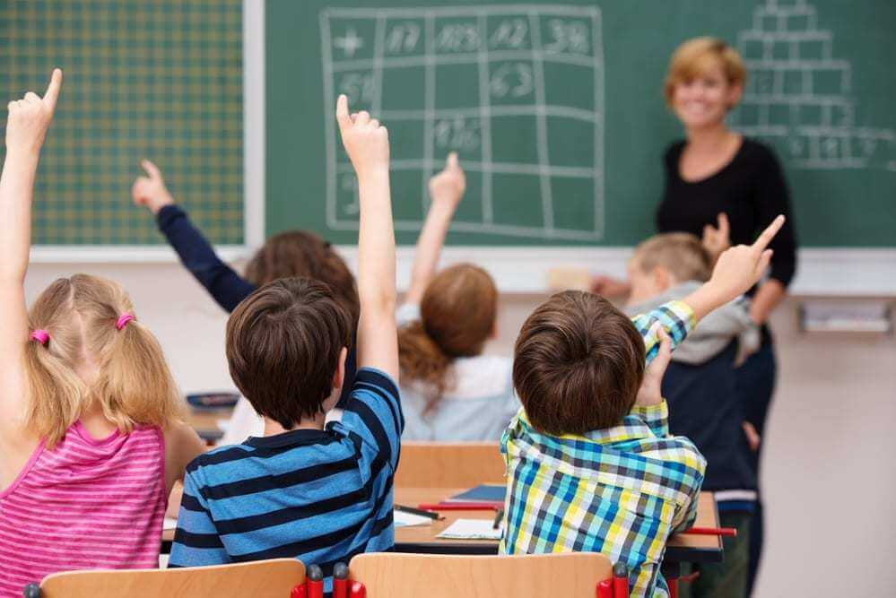 young school children all raising their hands to answer a question