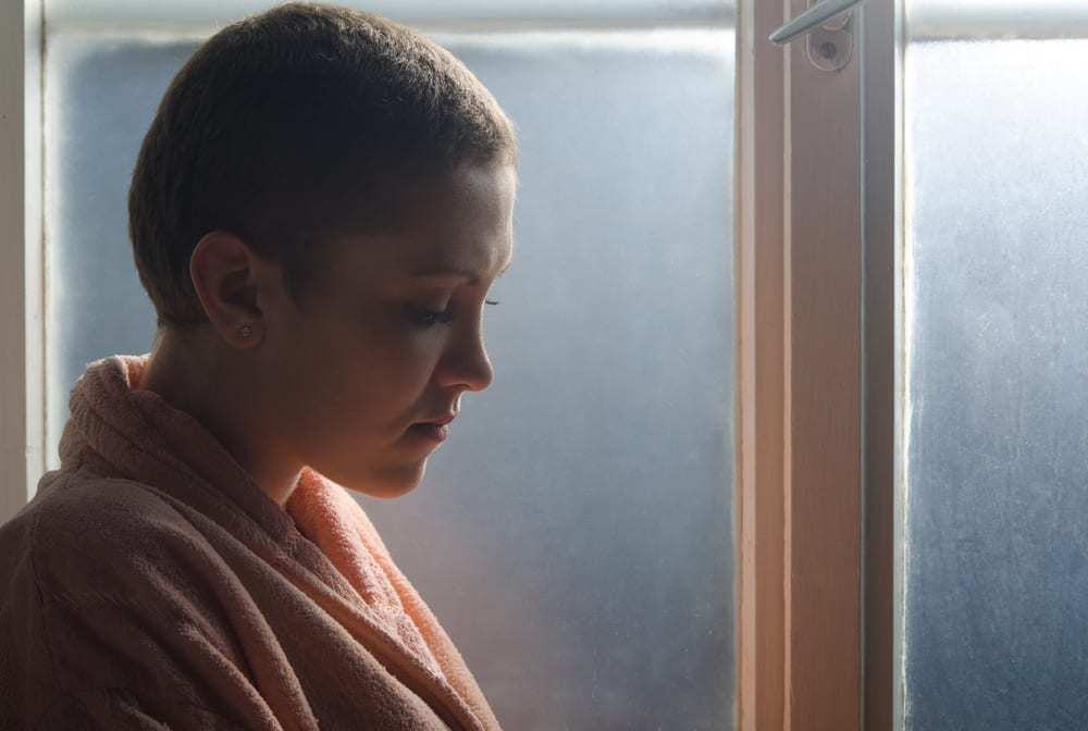 Young cancer patient standing in front of hospital window.